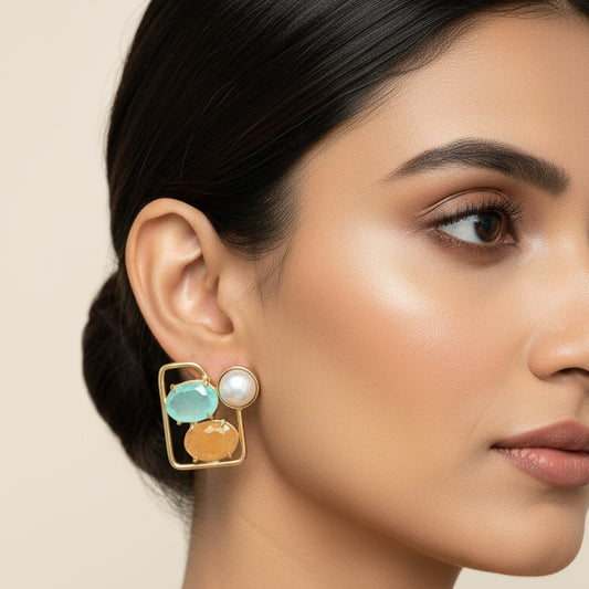 Pair of earrings with gold frames, turquoise stones, and pearls on a black card.