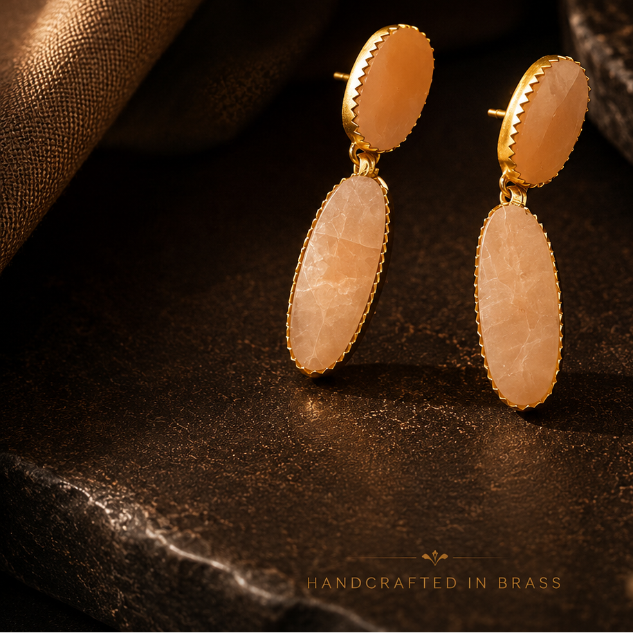 Gold and stone earrings on a dark surface with 'SURØBHI' branding.