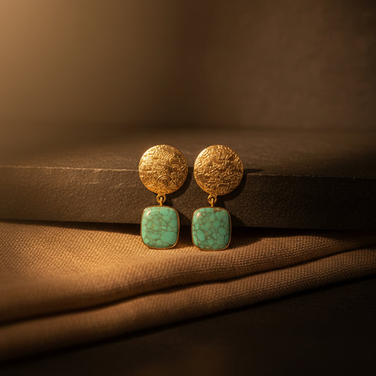 A pair of gold-toned dangle earrings with textured circular studs and square turquoise-blue stone drops, shown on a solid black background.