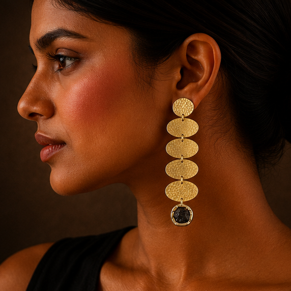 Gold-toned drop earrings with textured circular disc links and dark oval stones, shown on a display stand, worn by a model, and in a close-up detail shot against a dark brown background.