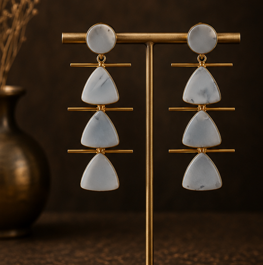 Three-panel product photo of statement dangle earrings. The left panel shows the earrings hanging on a gold display stand against a dark brown background.