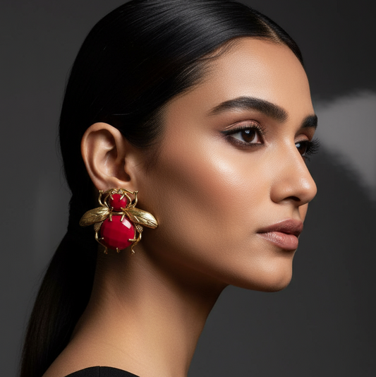 Woman wearing a red and brass earring  with a bug design 