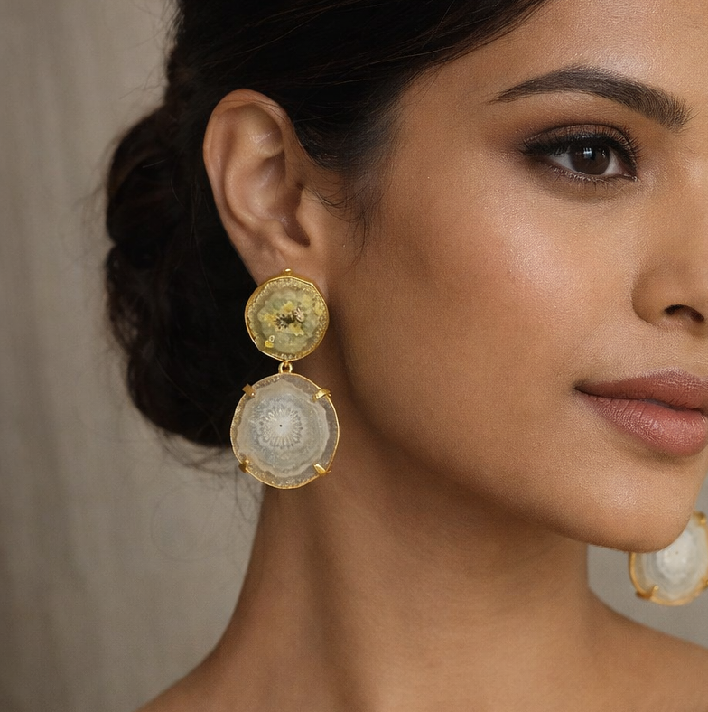 Woman wearing gold earrings and a gold saree against a neutral background