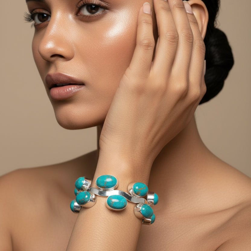 Hand wearing a silver bracelet with turquoise stones on a tiled floor.