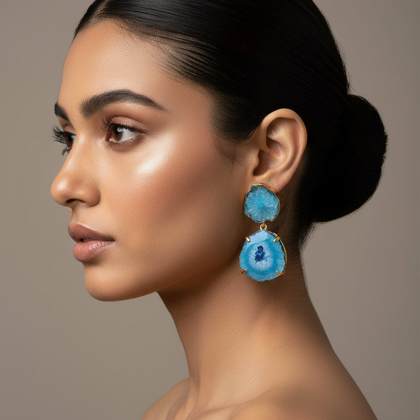 Blue geode-style earrings on a textured green and blue fabric background