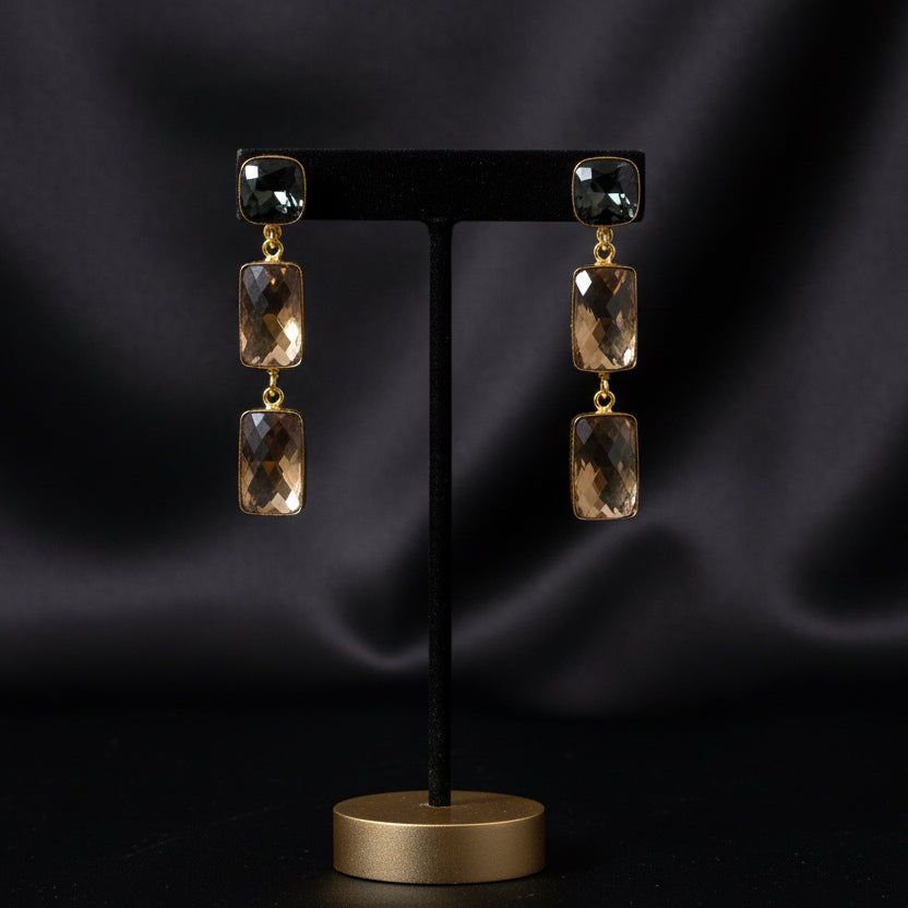 Pair of gold and smoky quartz earrings on a green fabric background