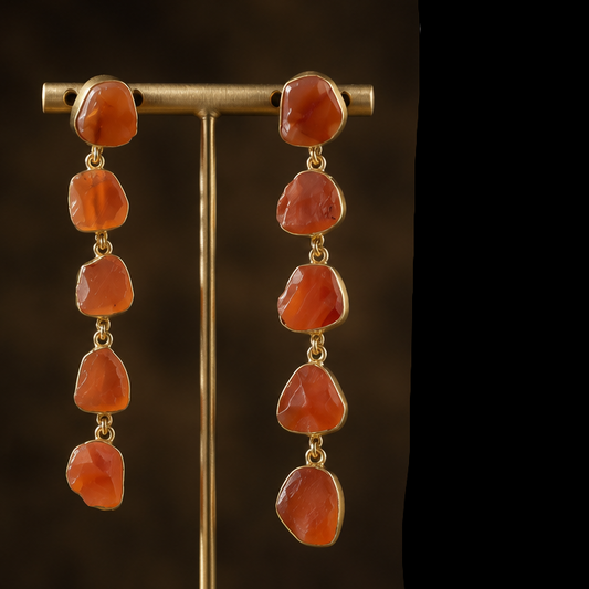 A three-panel collage showcasing a pair of gold drop earrings with orange stone beads. The left panel shows the earrings on a gold display stand, the center panel shows a woman wearing one earring, and the right panel shows the earrings on a dark textured background.